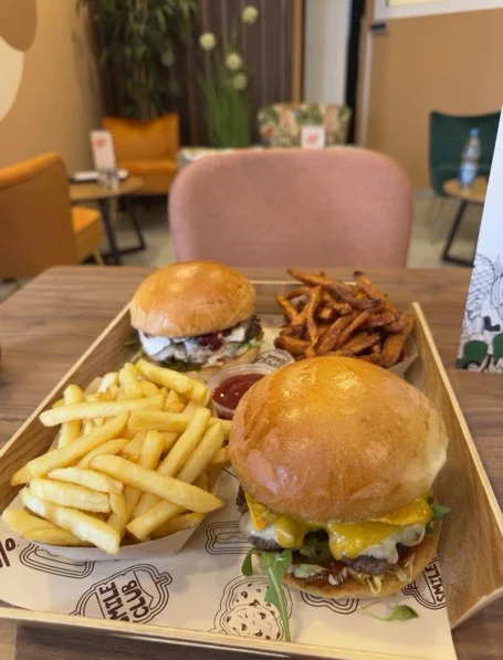 Zwei Burger mit Pommes und Süßkartoffel-Pommes auf dem Holztablett im Lokal
