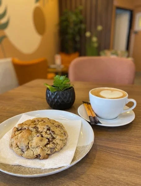 Cookie auf dem Teller und Cappuccino mit Herz-Latte-Art am Tisch im Lokal