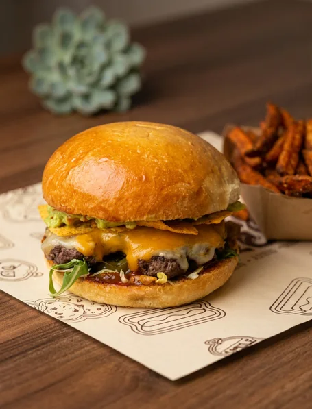 Cheeseburger mit Guacamole und Nachos, daneben Süßkartoffel-Pommes